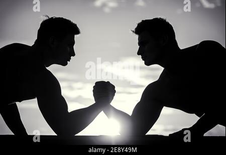 Rivalité, vs, défi, lutte de main. Coucher de soleil, lever du soleil. Silhouette de mains qui rivalisent en force. Rivalité, gros plan de lutte de bras mâle. Noir Banque D'Images