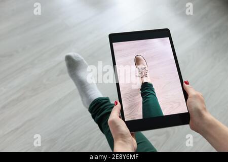 Femme tenant une tablette au-dessus de sa jambe et essayant des chaussures gros plan Banque D'Images