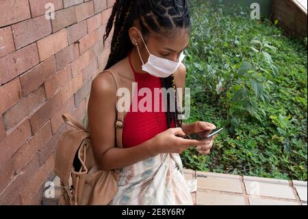 Jeune afro latina femme dans un masque facial utilisant son smartphone dans la rue, Colombie Banque D'Images