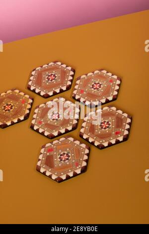 Sous-verres inlamés de marqueterie vintage aux couleurs marron et beige. Un motif oriental éclectique fait de bois de mosaïque sur une table ocre et un dos rose Banque D'Images