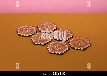 Sous-verres inlamés de marqueterie vintage aux couleurs marron et beige. Un motif oriental éclectique fait de bois de mosaïque sur une table ocre et un dos rose Banque D'Images