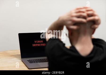 Virus détecté avec un signe d'avertissement en rouge sur un ordinateur portable. Un homme désespéré assis devant son ordinateur piller le texte sur son écran. Cybercriminalité Banque D'Images