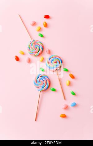 Les sucettes colorées tourbillonnaient sur les bâtonnets et les jelly beans. Bonbons multicolores en spirale à rayures sur fond rose, vue du dessus Banque D'Images