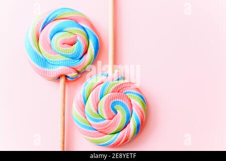 Des sucettes colorées tourbillonnaient sur des bâtons. Bonbons multicolores en spirale à rayures sur fond rose, vue du dessus Banque D'Images