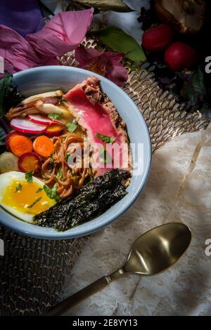 Ramen de thon ahi rose saisi garni d'œufs durs doux bandes d'algues radis et carottes en tranches multicolores Banque D'Images