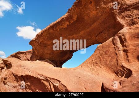 Petite formation d'arc ou de petite fenêtre de roche dans le désert de Wadi Rum, le soleil brillant brille sur la poussière rouge et les rochers, ciel bleu au-dessus Banque D'Images