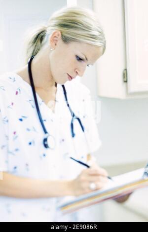 Une employée médicale écrivant sur un presse-papiers dans un environnement clinique. Banque D'Images