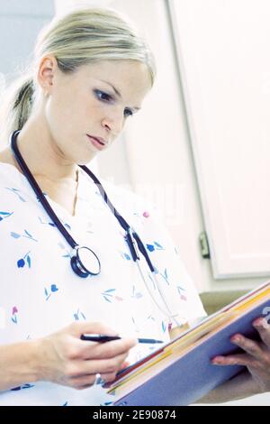 Une employée médicale écrivant sur un presse-papiers dans un environnement clinique. Banque D'Images