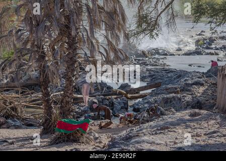 Femme imba non identifiée lavant des vêtements à Epupa Falls, Kunene River, Namibie Banque D'Images