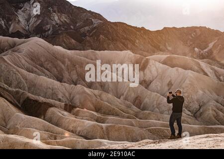 Homme prenant des photos sur un téléphone portable à Zabriskie point dans le parc national de la Vallée de la mort, Californie, États-Unis. Banque D'Images