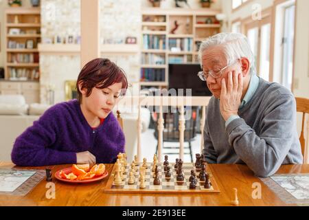 Un garçon aux cheveux rouges teints est assis à la table avec grand-père jouant aux échecs Banque D'Images