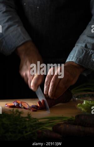 Un gros plan d'un chef hacher une carotte pourpre sur une planche à découper en bois. Banque D'Images