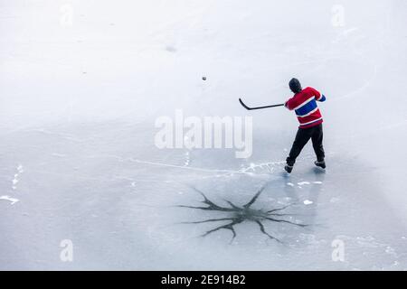 D'un homme anonyme en uniforme de tir de rondelle avec bâton en jouant au hockey près de crack dans la glace du lac gelé en Colombie-Britannique, Canada Banque D'Images