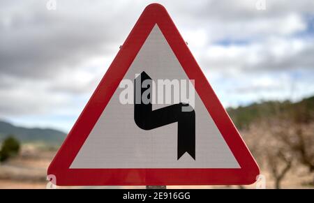 détail d'un panneau de signalisation triangulaire représentant un virage serré, avec une bordure rouge et un fond blanc Banque D'Images