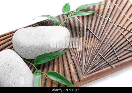 Planche avec aiguilles d'acupuncture et pierres de spa sur fond blanc, gros plan Banque D'Images