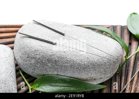 Planche avec aiguilles d'acupuncture et pierre de spa sur fond blanc, gros plan Banque D'Images