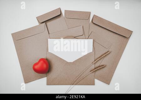 Le papier blanc vierge est placé sur l'enveloppe en papier brun ouvert avec un cœur rouge et une fleur sèche de queue d'bœuf sur fond blanc. Le cadeau de la Saint-Valentin Banque D'Images
