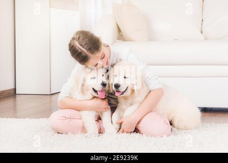 Une fille souriante s'assoit sur la moquette pour s'embrasser les chiots de la petite peluche à la maison Banque D'Images