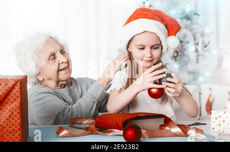 Petite-fille souriante dans le chapeau de père noël assis avec des boules décoratives à Noël Banque D'Images