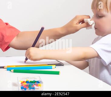 Une mère souffle son nez à une fille de 3 ans qui tire avec des crayons. Rhume et allergies chez les enfants Banque D'Images