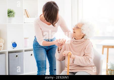 Une femme gentille aidant une vieille dame charmante à se tenir debout de la chaise Banque D'Images