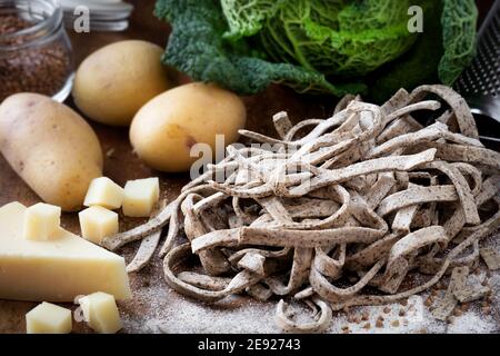 Pizzoccheri alla Valtellinese ingrédients - pâtes de sarrasin, pommes de terre, fromage, chou et beurre sur table en bois rustique foncé Banque D'Images