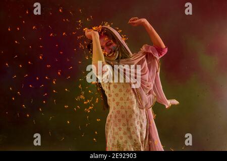Femme dansant avec des pétales de fleur autour d'elle sur Holi Banque D'Images