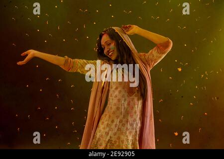 Femme dansant avec des pétales de fleur autour d'elle sur Holi Banque D'Images