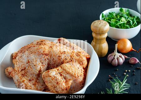 Poulet cru entier avec des ingrédients d'herbes et d'épices au four plat en céramique sur fond sombre prêt à cuire Banque D'Images