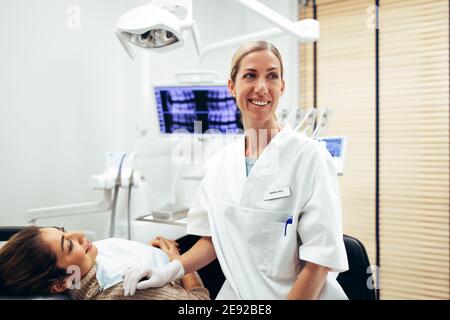 Une femme dentiste heureuse regardant quelque chose avec une patiente assise sur la chaise du dentiste. Dentiste heureux et patient à la clinique dentaire. Banque D'Images