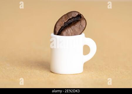 Gros plan d'une petite tasse de café blanc avec un grain de café sur un fond de papier kraft flou. Prise de vue en studio, mise au point sélective. Banque D'Images