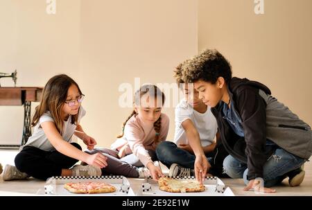 Groupe d'enfants très multiraciaux petits garçons filles s'assoient à l'intérieur de manger pizza cuisine italienne fast food. Tranches de partage de génération alpha, passer du temps Banque D'Images