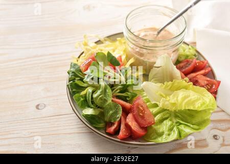 Salade fraîche de différentes laitues et tomates avec vinaigrette Thousand Island dans un pot en verre sur une assiette et sur une table en bois peinte en blanc, saine et crue Banque D'Images