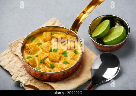 Poulet Korma dans un récipient en cuivre sur une table en béton gris. Cuisine indienne plat de cari à la viande avec masala au lait de coco. Cuisine asiatique Banque D'Images