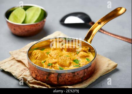 Poulet Korma dans un récipient en cuivre sur une table en béton gris. Cuisine indienne plat de cari à la viande avec masala au lait de coco. Cuisine asiatique Banque D'Images