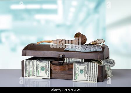 Une ancienne poitrine en bois remplie de 100 dollars US et une pipe à tabac et des lunettes sur le dessus se tiennent sur une table sur un fond flou lumineux. Entreprise et Banque D'Images