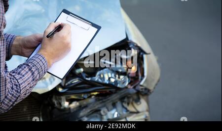 Les mains des hommes avec papier maquette d'assurance automobile vierge contre la voiture détruite dans un accident de la circulation. Bris du phare automatique avant. Durée de vie automatique et Banque D'Images