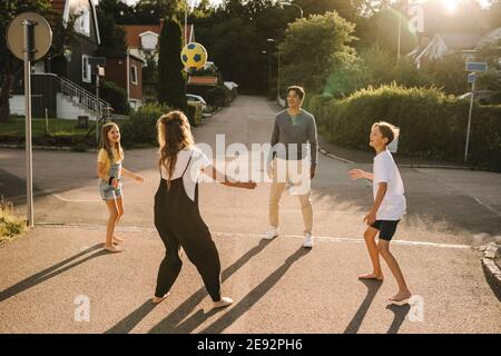 Bonne famille jouant avec le ballon de football sur la route Banque D'Images