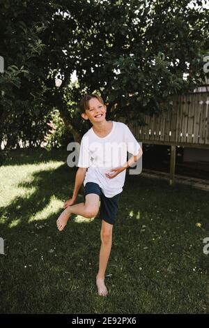 Joyeux garçon avec une jambe debout dans la cour arrière Banque D'Images Joyeux garçon avec une jambe debout dans la cour arrière Banque D'Images