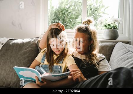 Fille écrivant dans le livre tout en étant assise par la mère sur le canapé à la maison Banque D'Images