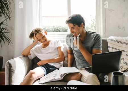 Père souriant assis par son fils avec livre sur le canapé séjour Banque D'Images