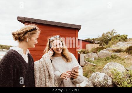 Jeune femme mettant bluetooth dans l'oreille d'un ami souriant contre le cottage Banque D'Images