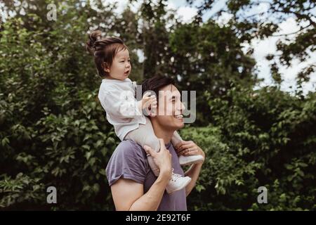 Père heureux portant bébé fils sur l'épaule par des arbres à l'intérieur stationnement Banque D'Images