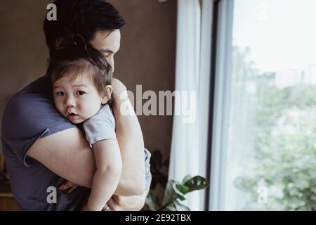 Père portant bébé fils par fenêtre à la maison Banque D'Images