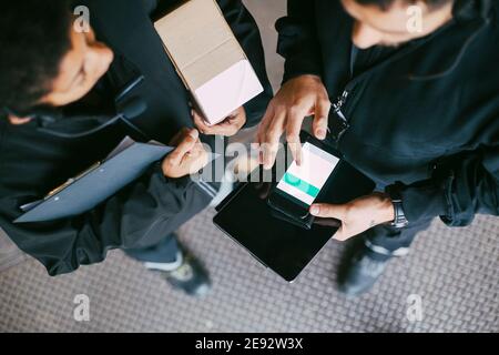 Vue en grand angle des collègues de sexe féminin et masculin utilisant la mobilité téléphone à l'entrepôt de distribution Banque D'Images