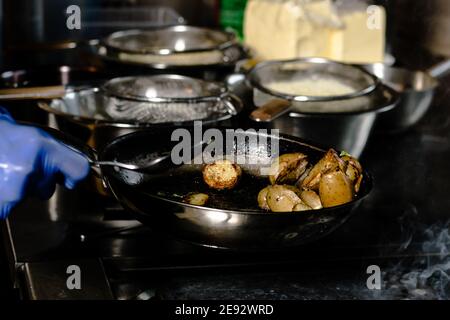 Chef friture des quartiers de pommes de terre sur une poêle en fonte à un restaurant Banque D'Images