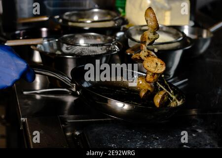 Chef friture des quartiers de pommes de terre sur une poêle en fonte à un restaurant Banque D'Images