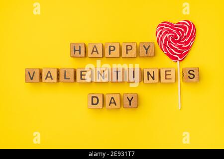 Cubes en bois avec l'expression « Happy Valentine's Day » sur fond jaune coloré vide. Les mots d'amour sont faits de lettres de bois pour la Saint-Valentin et pour votre petite amie, petit ami, femme, mari saluant carte postale romantique. Flat lay, vue de dessus Banque D'Images