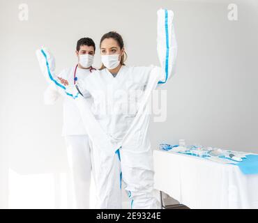 Medic aider la femme médecin dans le masque avec mettre sur la protection costume en se tenant dans la salle médicale blanche pendant une pandémie de coronavirus Banque D'Images