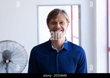 Portrait d'un homme caucasien souriant debout devant la fenêtre dans la salle blanche Banque D'Images